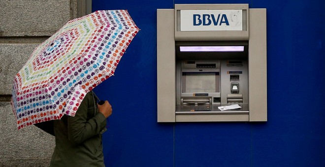 Una mujer con paraguas junto a un cajero automático de una sucursal de BBVA en Madrid. REUTERS/Andrea Comas