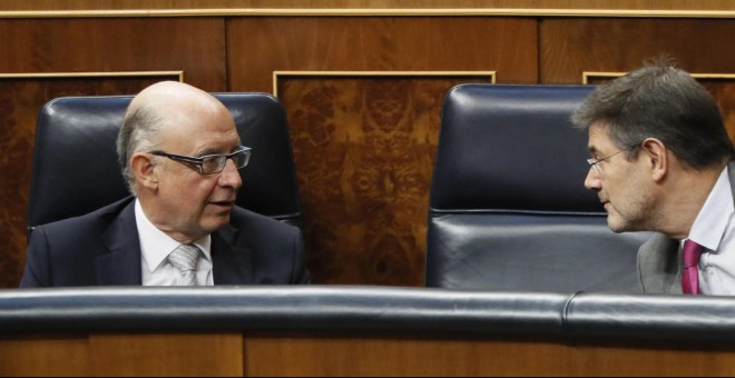 El ministro de Hacienda, Cristóbal Montero, conversa con el ministro de Justicia, Rafael Catalá, durante el Pleno del Congreso de los Diputados. EFE/ Fernando Alvarado
