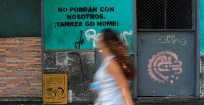 Mujer camina frente al mensaje de una de las paredes de Caracas - REUTERS
