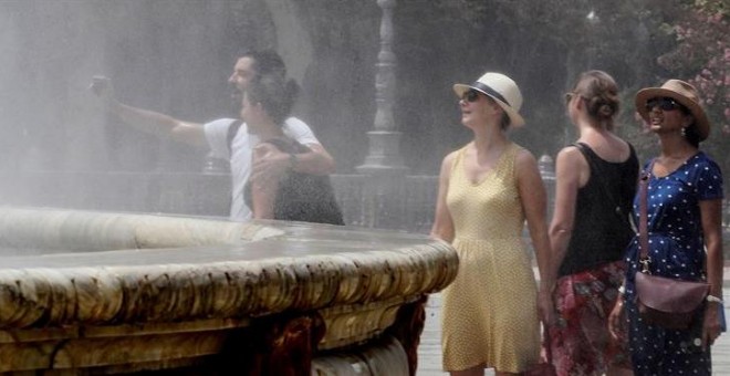 Turistas se refrescan en una fuente céntrica de Sevilla durante la ola de calor que azota España. / EFE