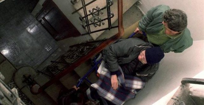 Un anciano discapacitado es ayudado para bajar la escalera de su vivienda - EFE