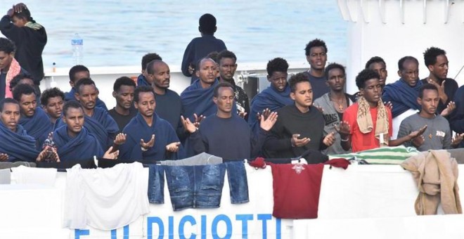 Migrantes rezan a la espera del desembarco del barco italiano de la Guardia Costera italiana en Catania. - EFE