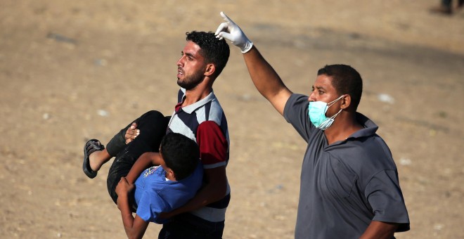 Dos hombres trasladan a un joven palestino herido durante las últimas protestas contra Israel. - REUTERS
