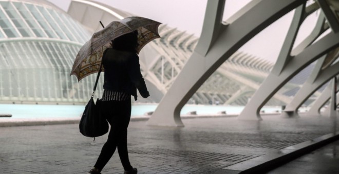 Una mujer se refugia de la lluvia con un paraguas en la Ciudad de las Ciencias de València./EFE