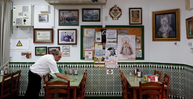 Un camareno limpia una mesa en el restaurante donde trabaja, en Chipiona (Cádiz). REUTERS / Marcelo del Pozo