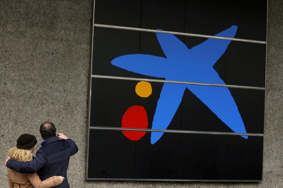 Una pareja se hace un selfi junto al logo de Caixabank en su sede en Madrid. REUTERS/Sergio Perez