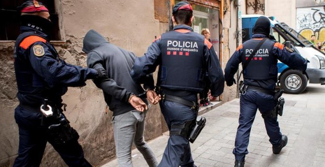 Los Mossos d'Esquadra custodian a uno de los detenidos en la operación contra el narcotráfico en Barcelona que incluye unos cuarenta registros de 'narcopisos'. /EFE