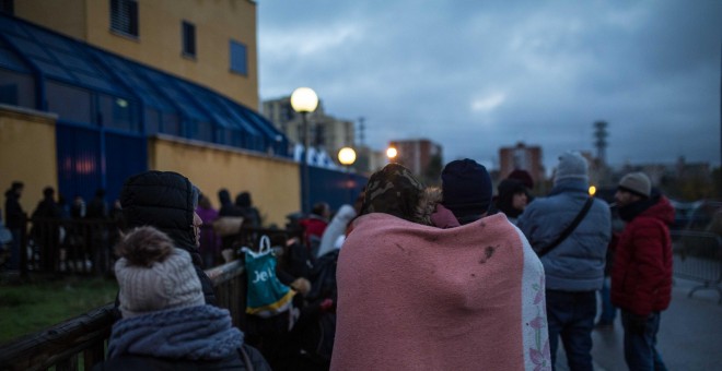 Una pareja de solicitantes de asilo se abriga con una manta mientras hace cola para pedir cita en la comisaría de Aluche. Algunos llevan 48 horas esperando su turno bajo el frío y la lluvia. JAIRO VARGAS