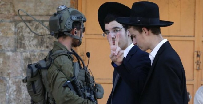 Dos colonos judíos pasan junto a un soldado israelí en Hebrón. - AFP