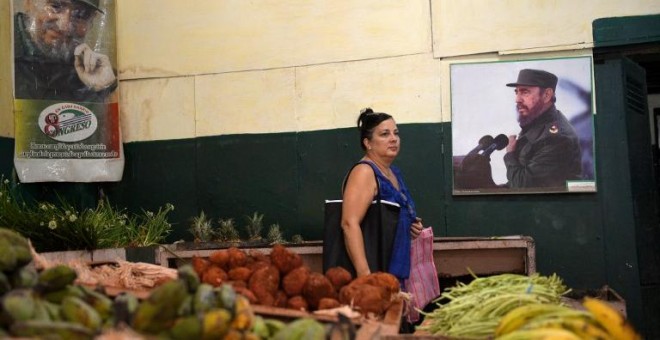 Una mujer compra verduras junto al póster del difunto líder cubano Fidel Castro en un mercado en La Habana. AFP/Yamil Page