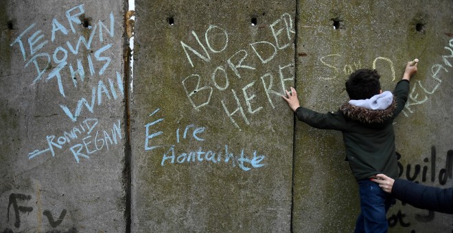 Un niño escribe un mensaje en un muro fronterizo simulado durante una protesta de activistas en contra del brexit, en Irlanda. | Reuters