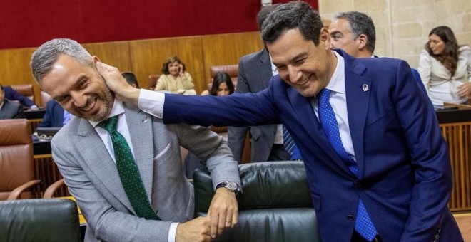 El presidente andaluz, Juanma Moreno, bromea con el consejero de Hacienda, Juan Bravo, al inicio del pleno del Parlamento de Andalucía. /EFE