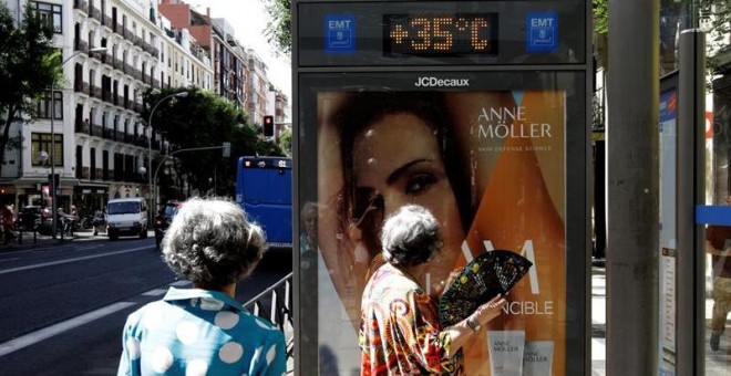 26/6/2019.- Dos mujeres que esperan la llegada del autobús observan los 35 grados que marca el termómetro de la marquesina a mediodía de hoy. La ola de calor, que comienza este miércoles, y que se prevé muy adversa por su intensidad, duración y extensión,