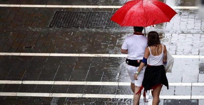 Dos personas se protegen de la lluvia en una de las céntricas calles de Pamplona durante la fiesta de San Fermín. Navarra está en alerta amarilla este lunes por lluvias y tormentas, según Aemet. EFE/ Javier Lizón