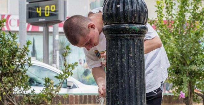 Un joven se refresca en una fuente de Murcia este medio día junto a un termómetro que marca 40º centígrados. EFE/Marcial Guillén