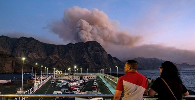 Dos personas observan al caer la tarde la columna de humo reactivada en el Pinar de Tamadaba que se ve desde el muelle de Agaete. EFE/Ángel Medina G.