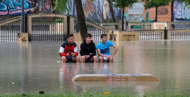 13/09/2019 - Tres jóvenes sentados en un banco en Orihuela pese a que las calles están inundadas por la gota fría. / REUTERS -  JON NAZCA