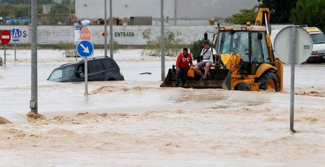 Dos ocupantes de un vehículo son rescatados con una pala mecánica, mientras la carretera permanece inundada por el efecto de las riadas, este viernes, en la ciudad alicantina de Orihuela, que se encuentra incomunicada, a causa del desbordamiento del río