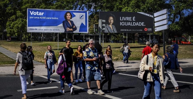 01/10/2019 - Personas cruzan una calle en Portugal ante pancartas electorales. / AFP - PATRICIA DE MELO MOREIRA