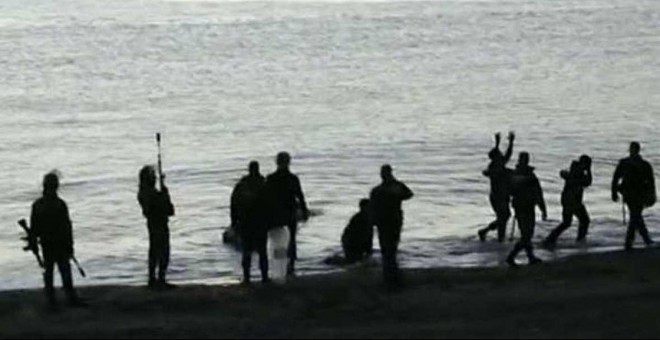 Algunos de los supervivientes en el momento de llegar a la costa ceutí entre guardias civiles provistos de material antidisturbio. - EFE