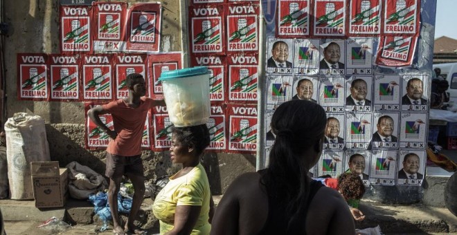Vendedores y clientes caminan por un muro cubierto con carteles de la campaña de las elecciones presidenciales de Mozambique en el mercado Xipamanine en Maputo. - AFP
