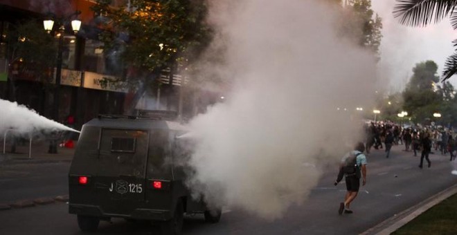 Carabineros de Chile rocía a los manifestantes con gas lacrimógeno este viernes en el marco de las protestas contra el alza del billete de Metro, en el centro de Santiago (Chile). Las protestas por el alza del precio del tiquete del Metro de Santiago se e