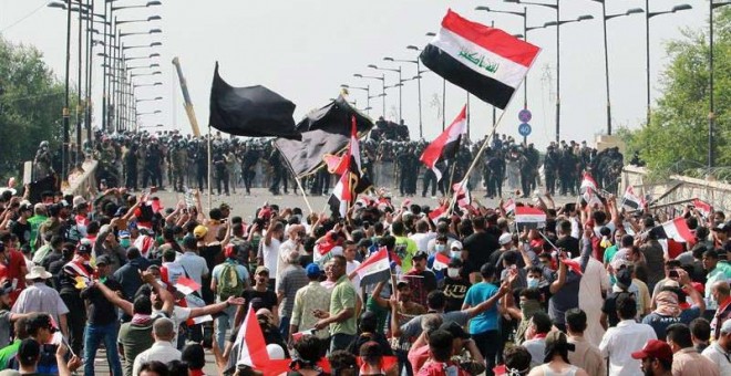Manifestantes iraquíes portan banderas nacionales mientras gritan consignas, este viernes durante una manifestación cerca de la sede central del gobierno iraquí, en el centro de Bagdad. (AHMED JALIL |EFE)