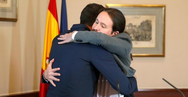 El presidente del Gobierno español en funciones, el socialista Pedro Sánchez, de espaldas, y el líder de Unidas Podemos, Pablo Iglesias, se abrazan en el Congreso de los Diputados donde firmaron un acuerdo para la formación de un Ejecutivo en España tras