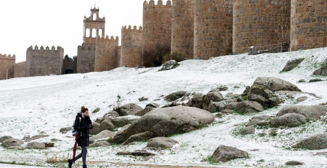 Una mujer camina junto al lienzo norte de la muralla de Ávila cubierta por una fina capa nieve caída en las últimas horas. EFE