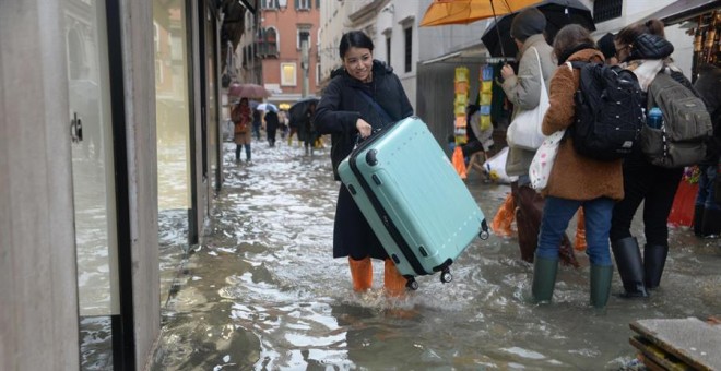 Una turista carga su maleta con ruedas para evitar que toque el 'agua alta' en Venecia (Italia), este viernes. EFE/Andrea Merola
