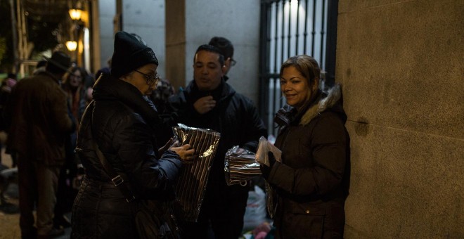 Una voluntaria reparte bufandas entre los solicitantes de asilo que esperan en las puertas del Samur Social de Madrid un plaza para pasar la noche.- JAIRO VARGAS