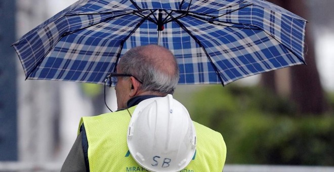 Un trabajador de la construcción se protege de la lluvia con un paraguas en Valencia. EFE/Kai Försterling