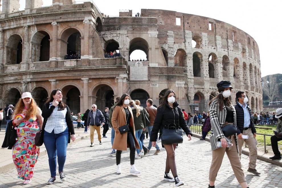 Turistas pasean junto al coliseo en Roma portando mascarillas. / Reuters