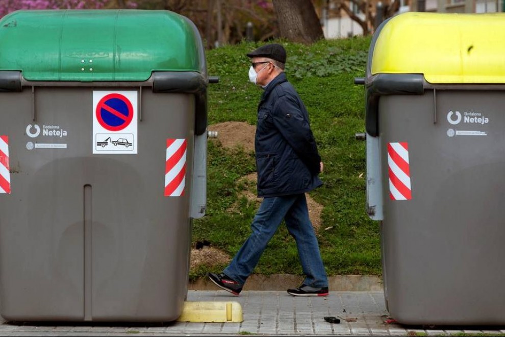 Un hombre camina junto a dos contenedores de basura.
