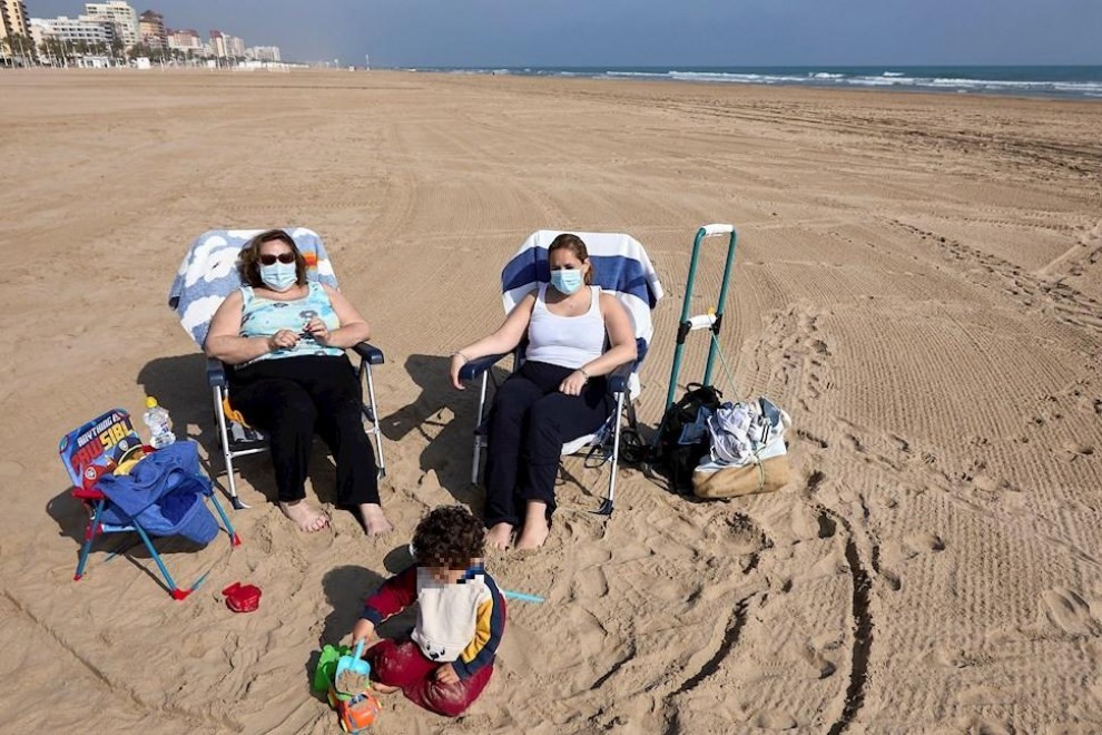 Varias personas toman el sol con mascarilla en la playa de Gandía.