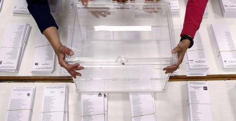 Tres personas sujetan una urna sobre las papeletas en un colegio electoral. EFE