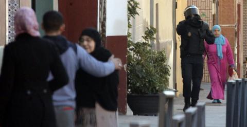 Un policía pasa junto a varios vecinos de la barriada de El Príncipe, donde la Policía española ha detenido esta madrugada a cuatro presuntos yihadistas, que, según el ministro del Interior, son dos parejas de hermanos 'fuertemente radicalizados', muy adi