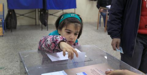 Una niña introduce en la urna el voto de sus padres en un colegio electoral en Atenas. EFE/EPA/SIMELA PANTZARTZI