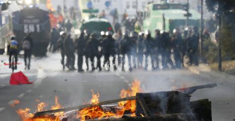 Un contenedor quemado en Fráncfort y de fondo una hilera de antidisturbios. /REUTERS