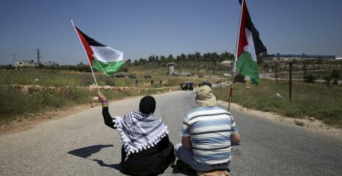 Protestantes palestinos sostienen banderas palestinas mientras militares israelíes toman posiciones durante una protesta contra los asentamientos ilegales en Cisjordania, al lado de Ramala./ REUTERS/Mohamad Torokman