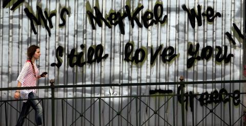 Una mujer pasa junto a una pintada en una calle de Atenas que, en inglés, dice 'Señora Merkel, todavía la queremos. Grecia'. EFE/EPA/SIMELA PANTZARTZI