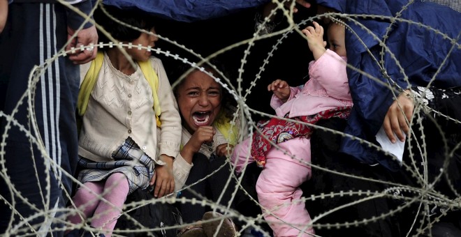 Una niña refuegiada llora tras la alambrada policial que les impide cruzar la frontera entre Grecia y Macedonia.- REUTERS
