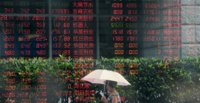 Una mujer pasa junto al ventanal de una firma de broker en Shanghai.  REUTERS/China Daily