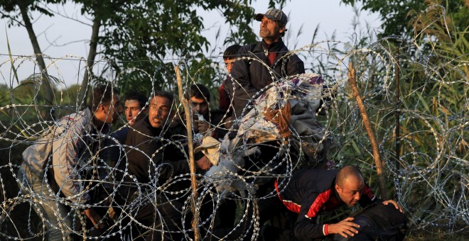 Refugiados sirios cruzan la valla de cuchillas que Hungría ha instalado en su frontera con Serbia, cerca Röszke.- REUTERS / Bernadett Szabo