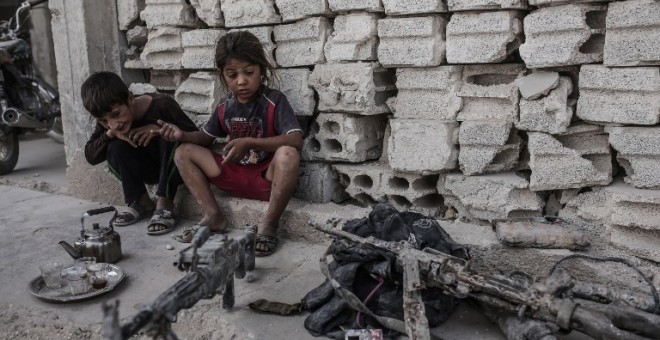 Dos niños permanecen en Kobani, Siria, junto a varias armas incautadas a combatientes del Estado Islámico. - AFP