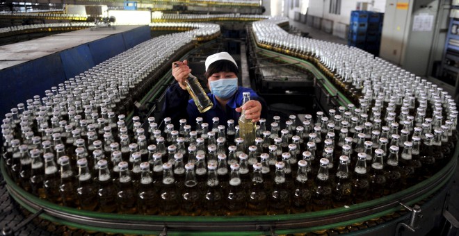 Una mujer recoge botellas de cerveza en una cadena de montaje dentro de una fábrica en Shenyang. REUTERS