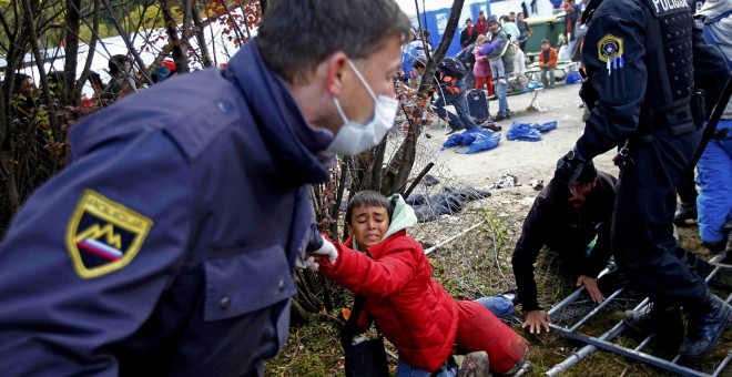 Un oficial de la policía eslovena levanta a un niño después de que una multitud de refugiados rompiera el cordón policial para escapar del campo de refugiados y llegas hasta Austria.- REUTERS / Leonhard Foeger