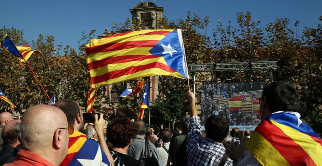 Miembros de la ANC y otras entidades soberanistas siguen, con estelades, a través de una gran pantalla instalada ante el Parlament el debate. /EFE