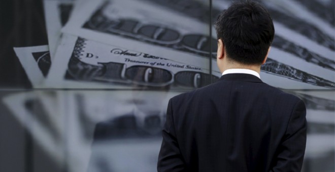 Un hombre de negocios japonés mira un escaparate en Tokio que muestra imágenes de los billetes de 100 dólares. REUTERS/Toru Hanai