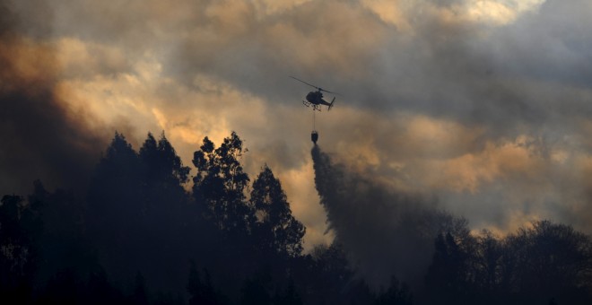 Un helicóptero suelta agua en el bosque de La Fresneda, cerca de Oviedo./ REUTERS/Eloy Alonso